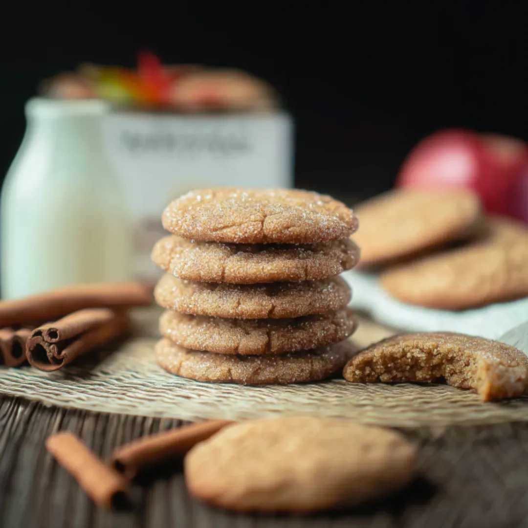 apple cider cookies with cinnamon sugar cookies beside a glass of milk and cinnamon sticks on a rustic table.